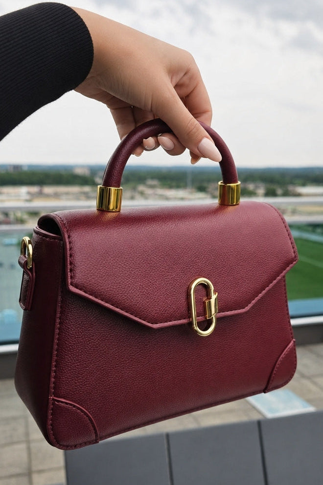 Burgundy handbag with gold accents held by a person against an outdoor background